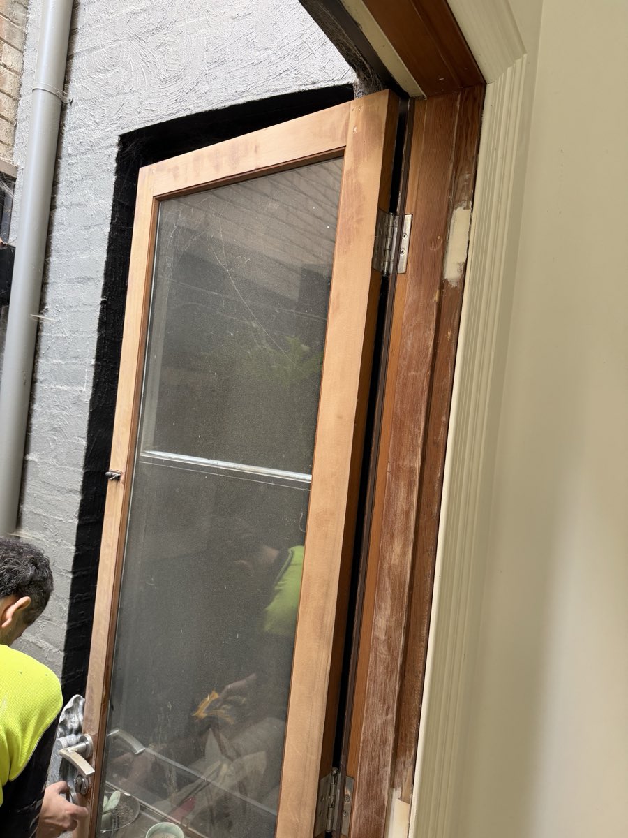 The same doorway during preparation: bare sanded timber on the door stiles and frame, with a painter partly visible at the edge of the frame.