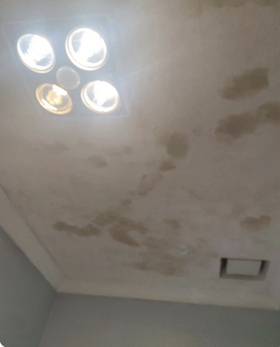 A ceiling before repainting, showing patchy brown staining around a light fitting and a ceiling vent.