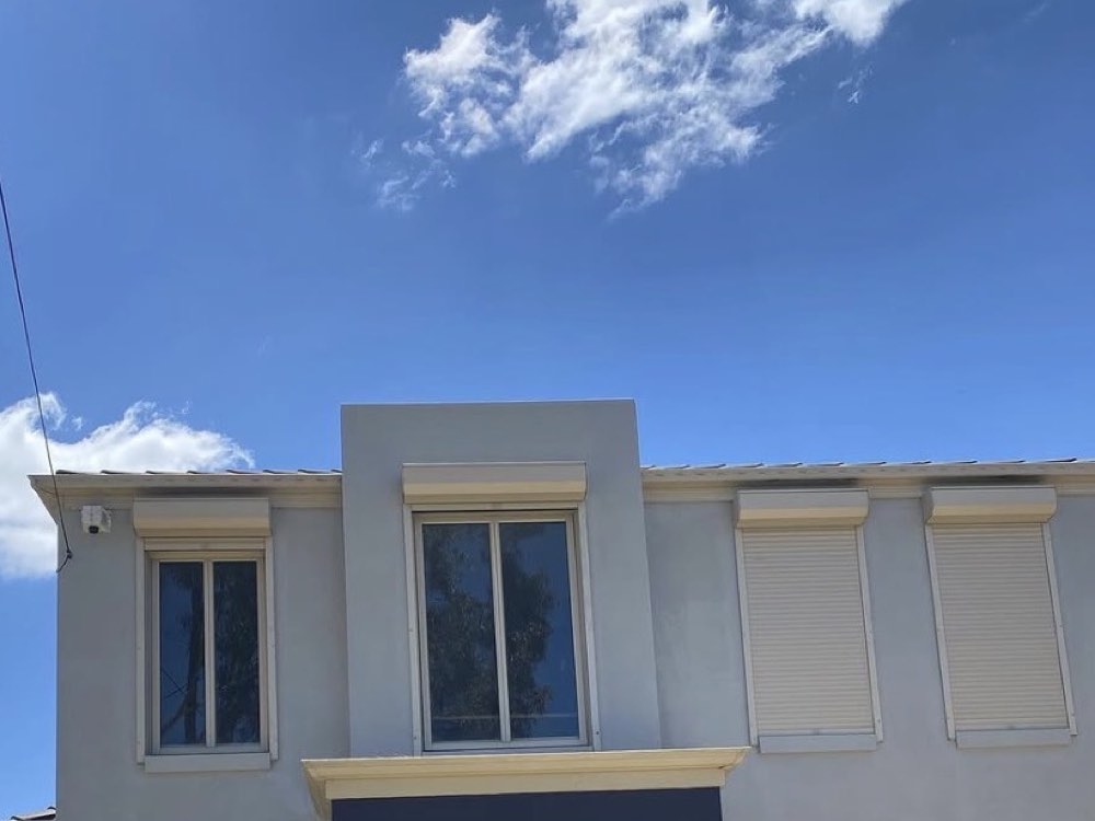 The same upper exterior facade after repainting, with a lighter wall finish and refreshed trim beneath a blue sky.