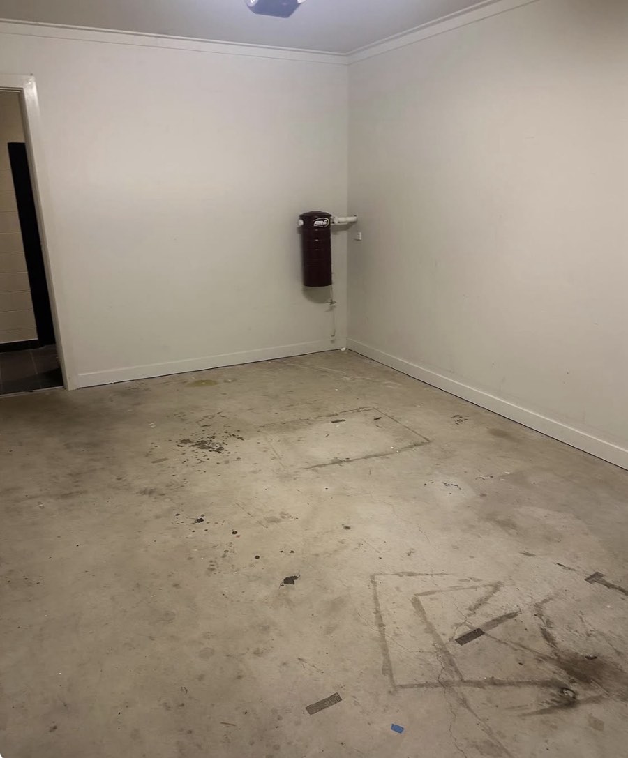 An empty garage or utility room before repainting, with marked concrete flooring and pale walls beside an open doorway.
