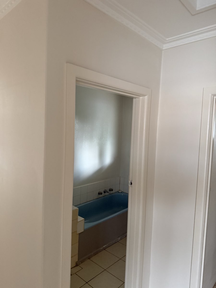 A light painted wall and doorway open toward a bathroom with a blue bath.