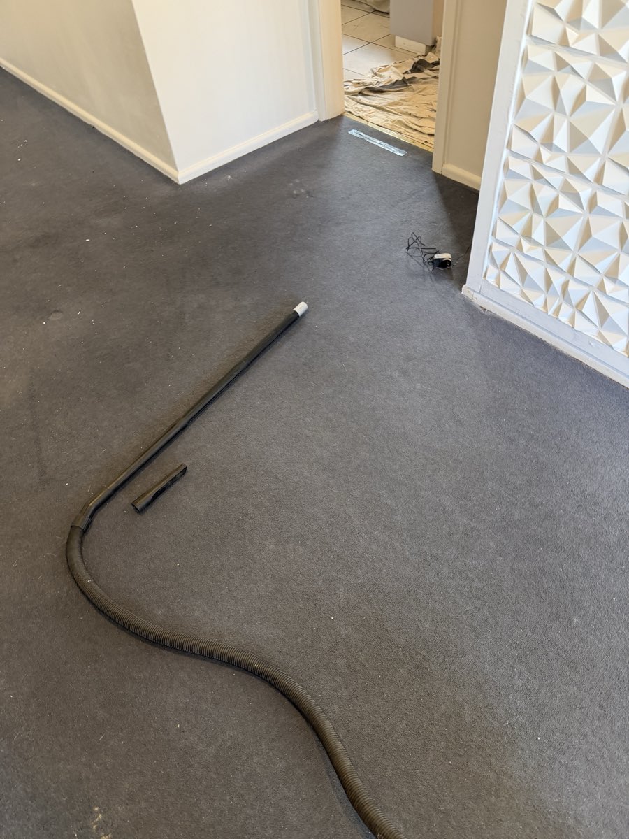 A vacuum hose lies across carpet during room cleanup after painting work.