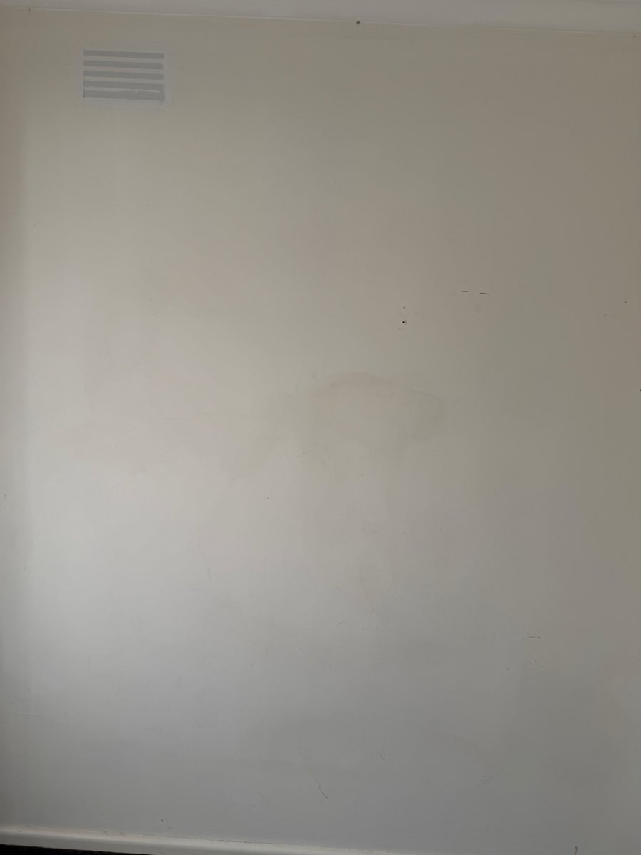 A pale interior wall shows scattered marks below a small rectangular wall vent.